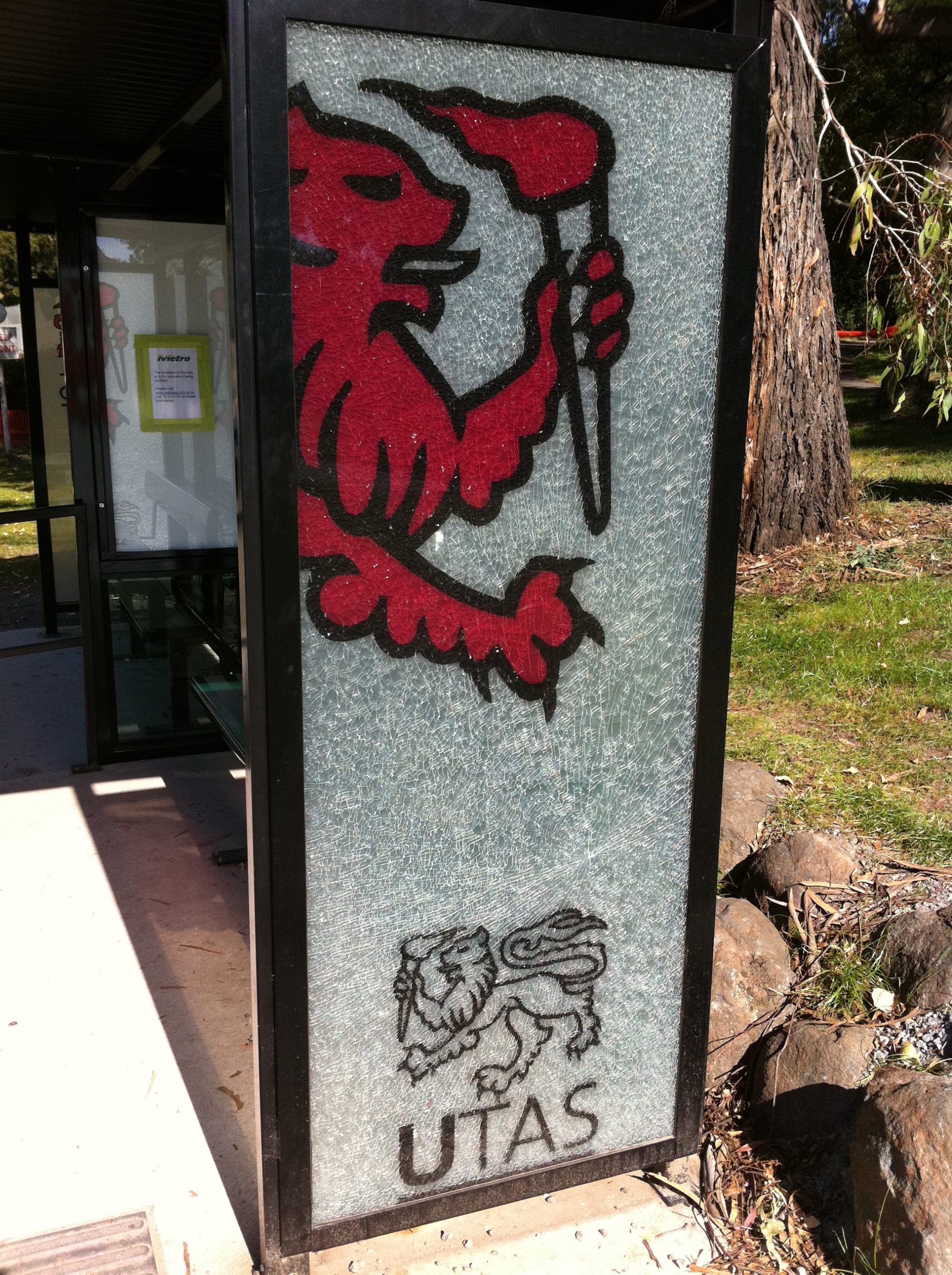 A smashed glass pane on a bus stop with the UTAS logo